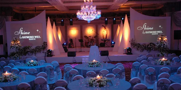 Corporate event setup with stage lighting, chandelier and round banquet tables