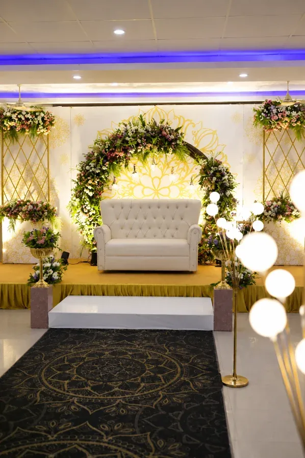 Wedding reception stage with a white settee, gold drapes and a floral arch inside the hall