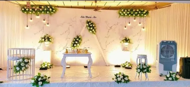Wedding reception stage with a marble-effect backdrop, white floral arrangements and hanging lights at S P Convention Center